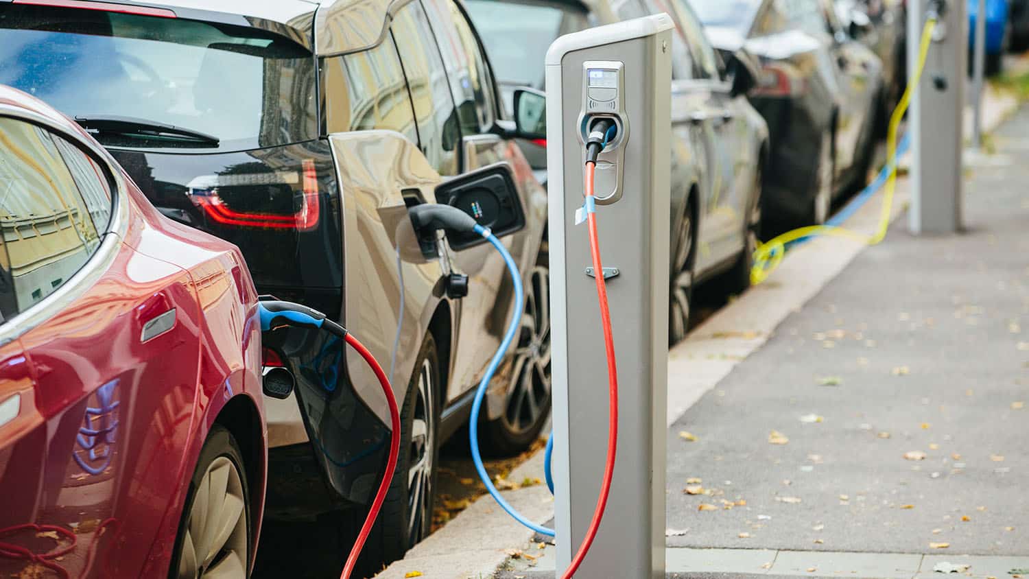 Several electric cars parked along a road, being charged by sidewalk charger posts